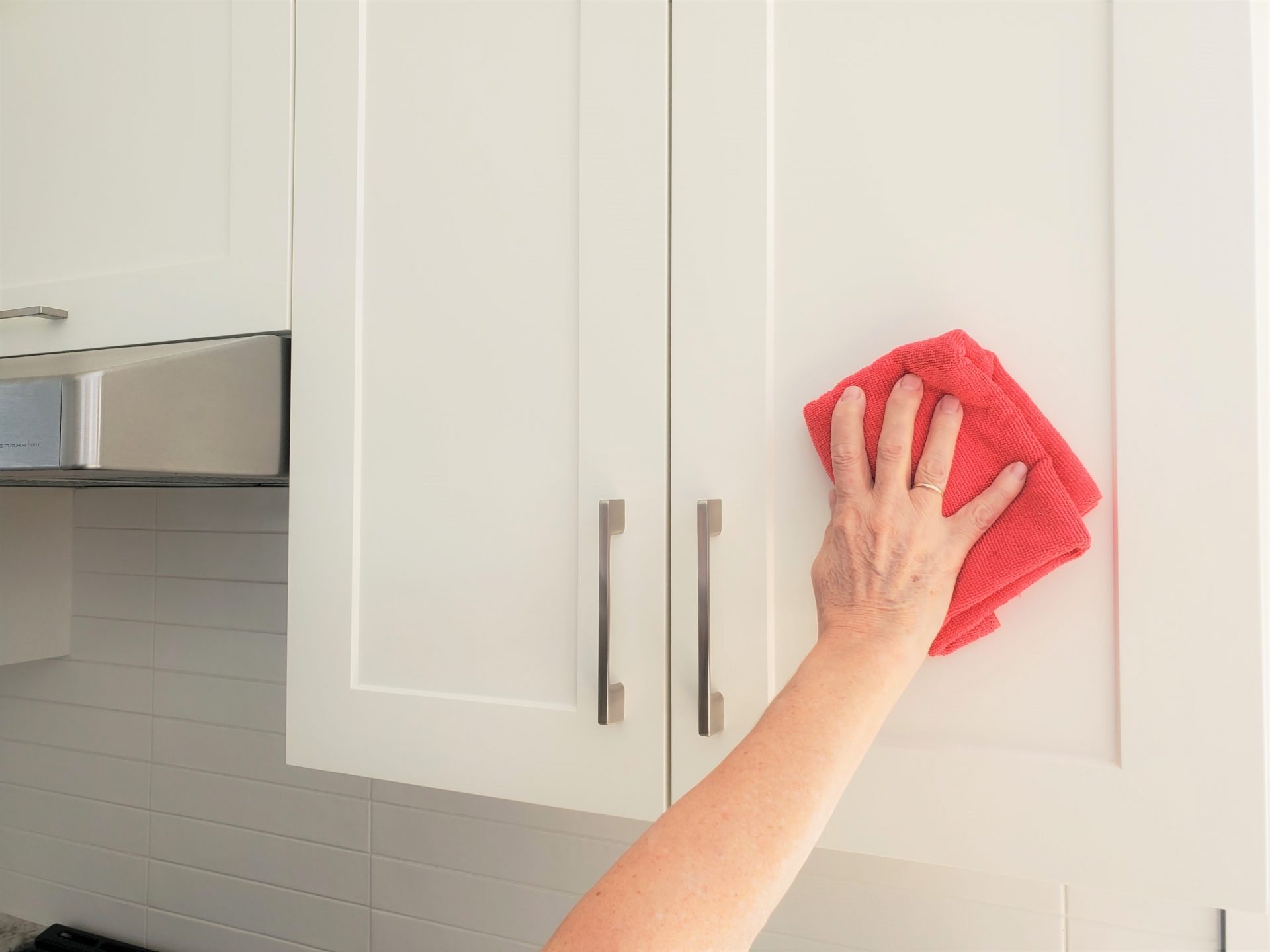 Une main essuie une porte d’armoire blanche avec un chiffon en microfibre rouge.