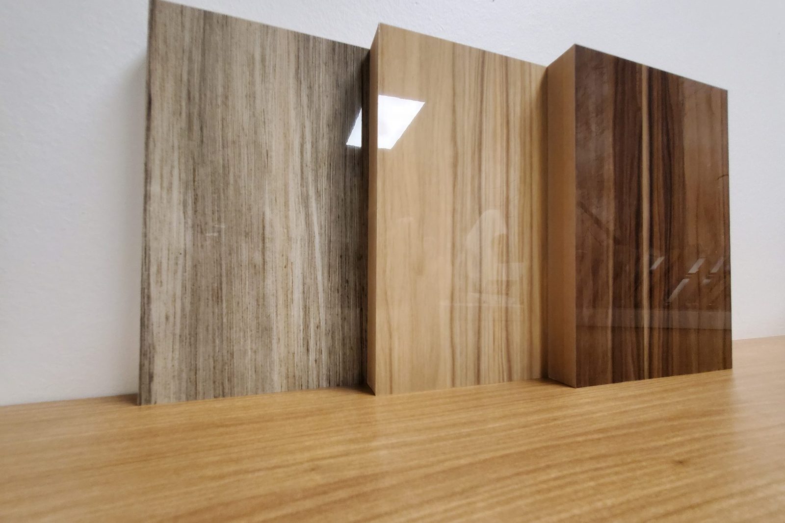 Les couleurs : trois panneaux de finis lustrés, gris veiné, chêne doré et noyer, posés sur un comptoir de bois