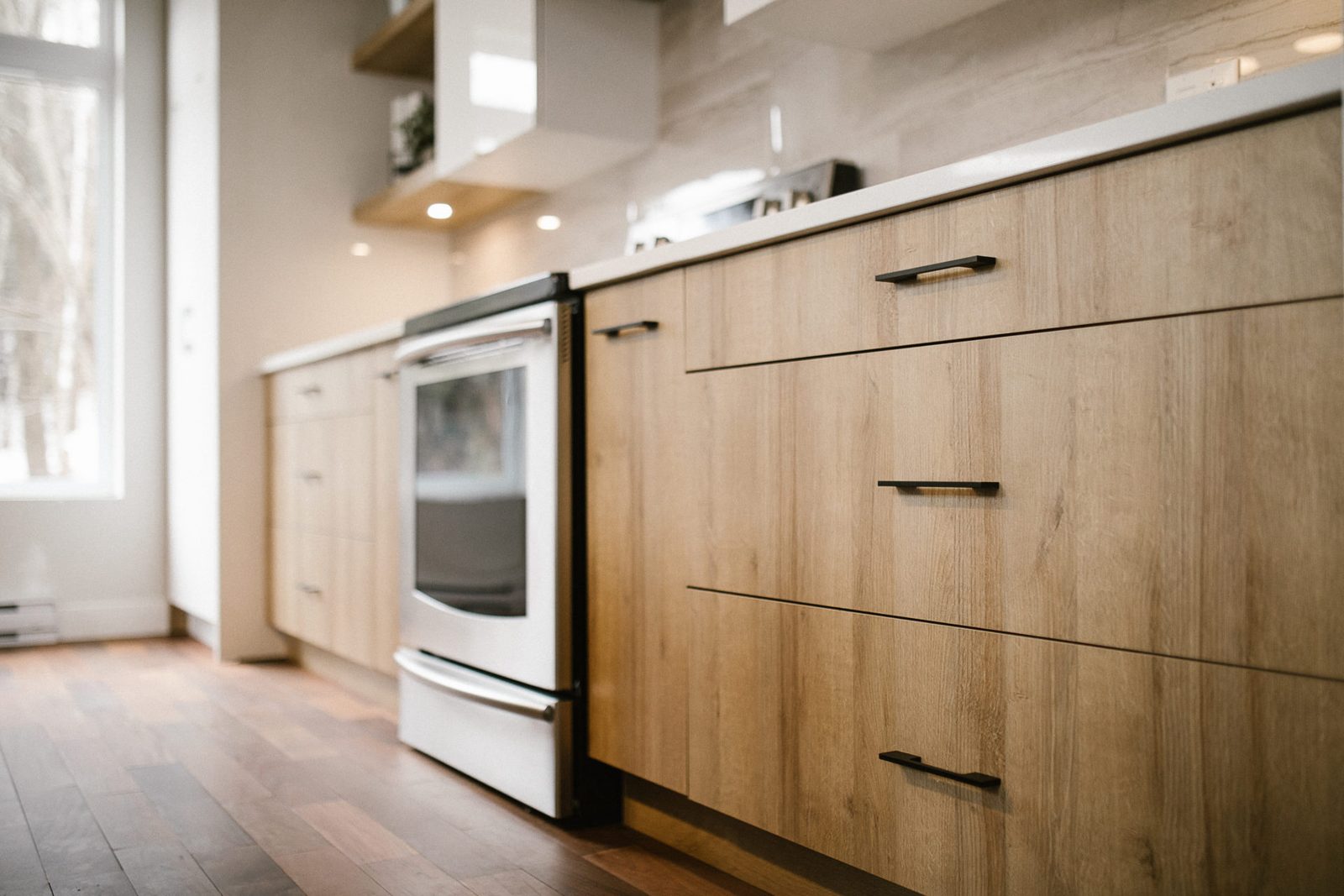 Collection Laminé : gros plan sur des tiroirs en laminé chêne clair, poignées noires, cuisinière blanche
