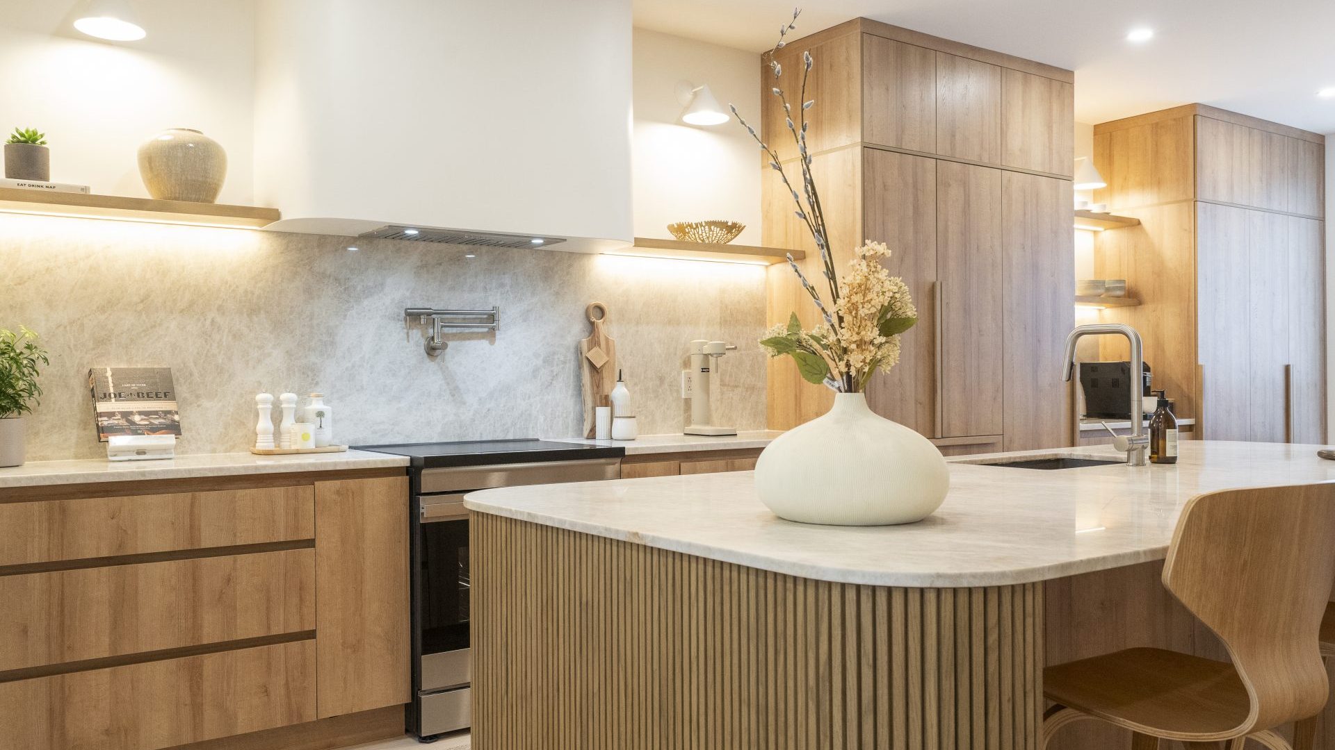 Une cuisine Luxor Collection : îlot cannelé en chêne clair, comptoir de quartz, armoires de chêne jusqu'au plafond, dosseret de pierre