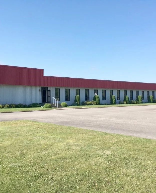 L’usine de Lachute : un long bâtiment au toit rouge, devant une pelouse, sous un ciel bleu.