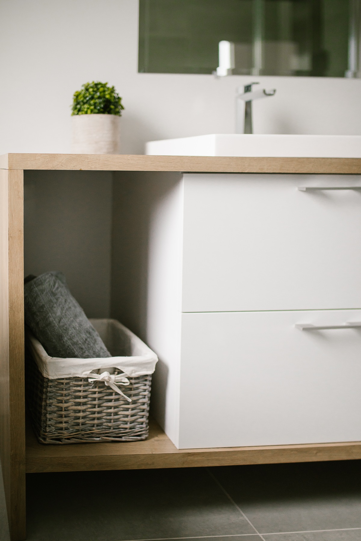 Meuble-lavabo blanc sur caisson de bois, panier tressé dans la niche ouverte.