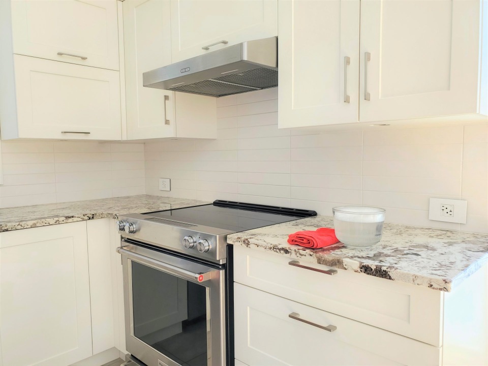 Coin de cuisine blanche : armoires, hotte et cuisinière, comptoir de granit.