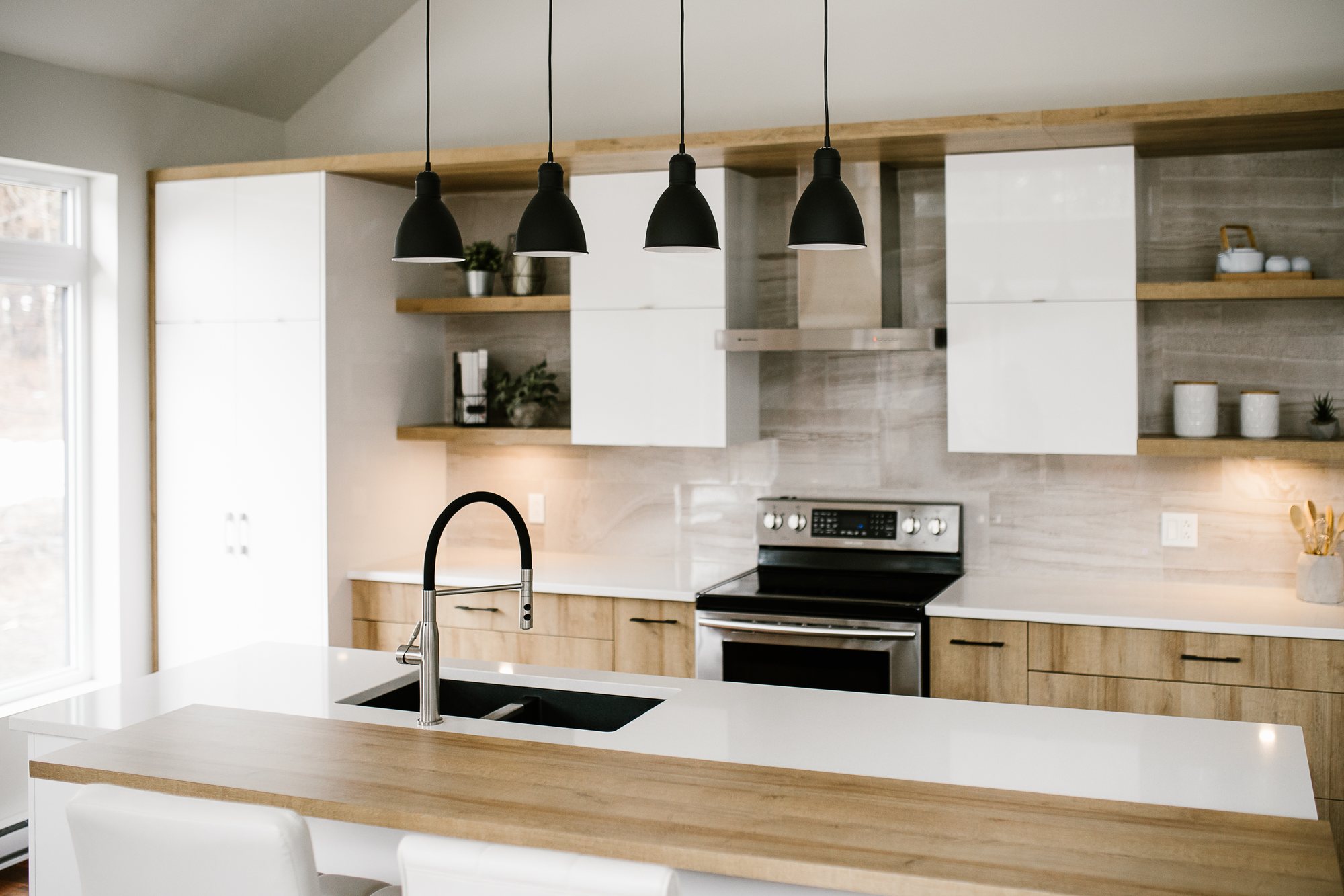 Cuisine en laminé blanc lustré et bois clair : îlot, tablettes ouvertes et quatre suspensions noires.