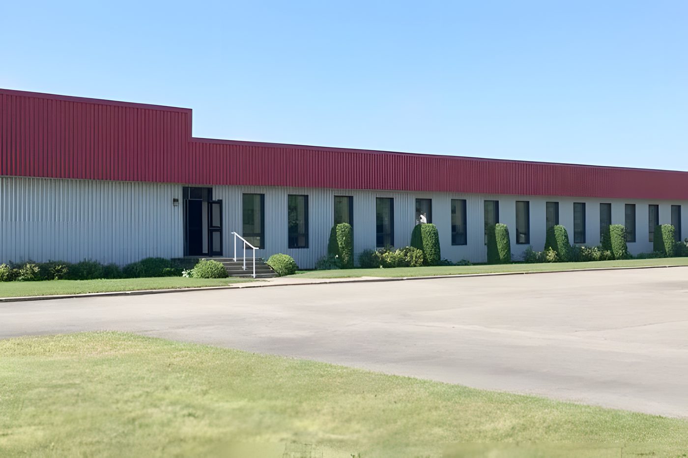 L'usine de Luxor Collection à Lachute : un long bâtiment au toit rouge, pelouse et stationnement, ciel bleu